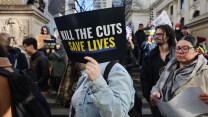 A group of people holding signs. One sign reads "Kill The Cuts Save Lives"