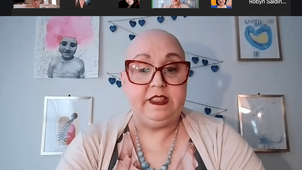 Screenshot of a Zoom window, showing a white woman with no hair wearing glasses with art above her. There are inset images of people above her.